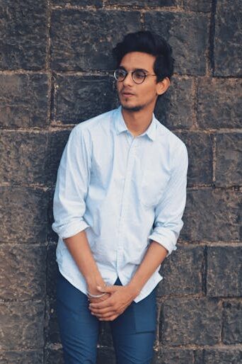 Stylish young man with eyeglasses posing against a brick wall outdoors.